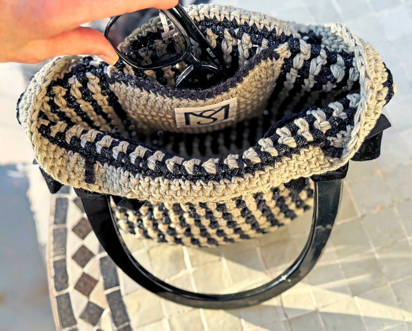 Feeling so French with daytime chic, Basque crochet tote. Up-cycled cotton blend and nylon yarns in a linear stripe pattern with velvet bows and large black Lucite handles to wear over your shoulder. Two interior pockets are ideal to store your phone and sunglasses. Dimensions: Height: 10" Length: 12" Width: 7" Handles: 6.5" x 6" high (inside of handle measurement) Spot treat with mild soap or dry clean Consciously made in California