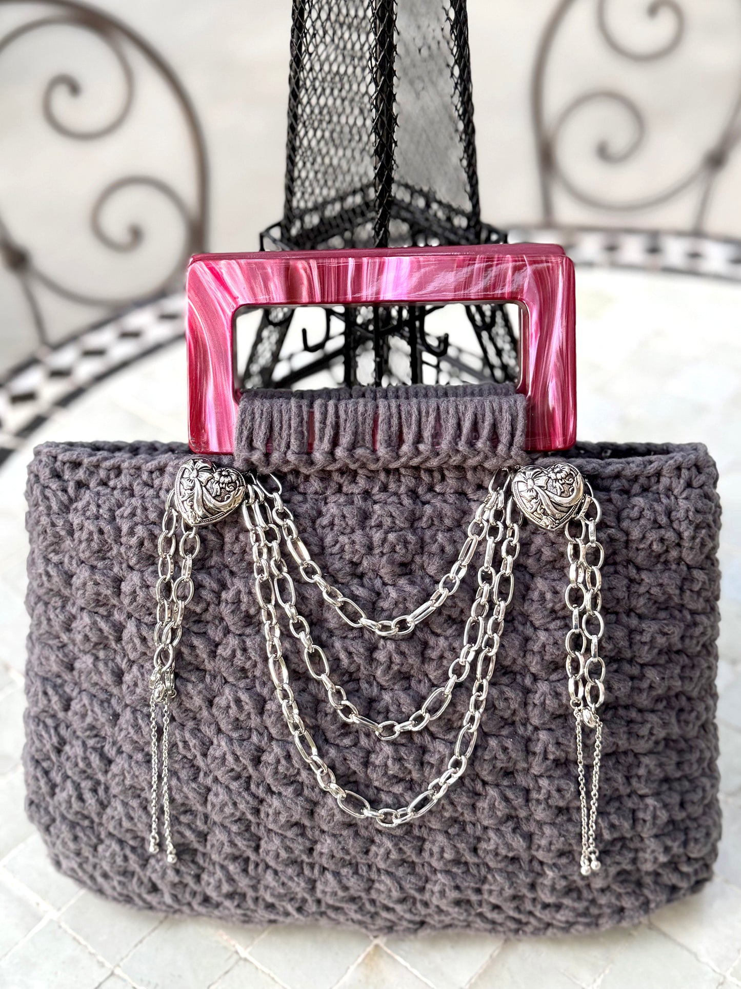 French is the language of Love, and the L'Amour vintage crochet bag reflects the beauty of European expert craftsmanship. Adorned with stainless steel chains, heart engraved buttons, and dark pink, marbled Lucite handles. High quality, upcycled acrylic yarn in slate gray, crocheted in a secure binding pattern, insures no lining is needed. Dimensions: 10" long, 10" high (including handles), 3.5" wide Dry Clean only Consciously made in California