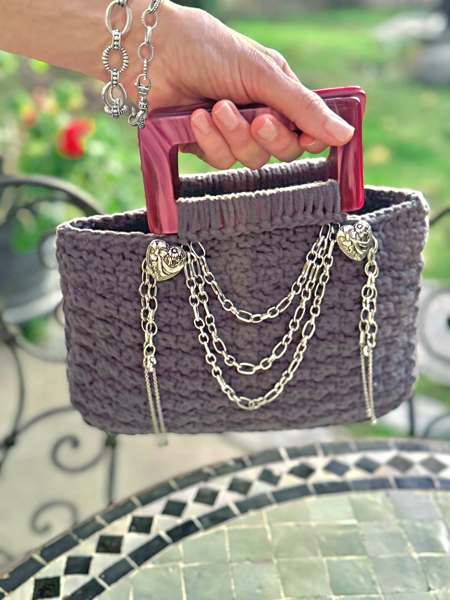 French is the language of Love, and the L'Amour vintage crochet bag reflects the beauty of European expert craftsmanship. Adorned with stainless steel chains, heart engraved buttons, and dark pink, marbled Lucite handles. High quality, upcycled acrylic yarn in slate gray, crocheted in a secure binding pattern, insures no lining is needed. Dimensions: 10" long, 10" high (including handles), 3.5" wide Dry Clean only Consciously made in California