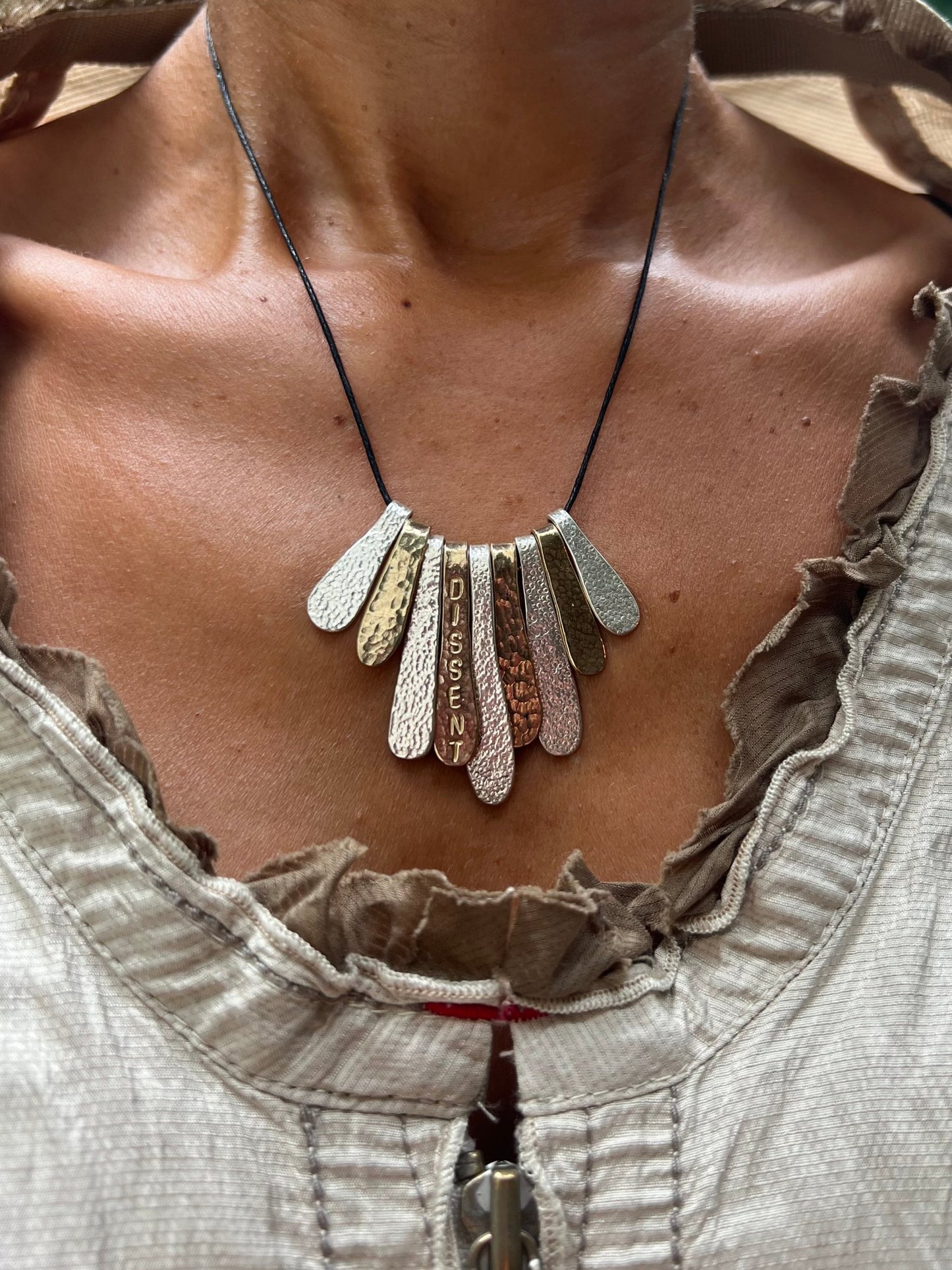 The handcrafted Dissent Necklace was inspired by Ruth Bader Ginsburg’s brilliance, power and commitment to justice. Each unique necklace has 9 hand stamped, texturized pieces made from sterling silver and brass. These pieces are individually filed, sanded, polished, softened by fire and curved to their final shape. Choose between silver chain or leather cord. Each piece is made to order and can take up to one week to ship. Clean with polishing pad or soft cloth and mild soap. Consciously made in New York