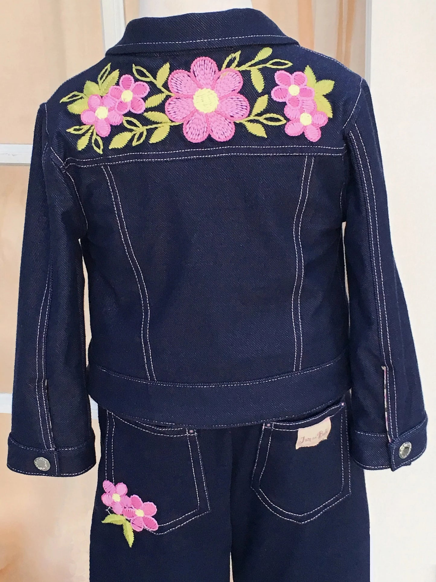 The softest denim jacket with embroidered pink daisies and pink top stitching. Fully lined with 100% cotton knit, in a pink stripe pattern. Hand-crocheted pink daisies appliqued on front of jacket. Nickel free, silver snap closures for easy on and off. Complete the look with a pair of Denim & Daisies Jeans and your little one will be the cutest dressed for line dancing. Order a size larger for longer wear Denim Knit - 85% Cotton, 15% Lycra Machine washable, cold, delicate cycle (inside out to protect embroi