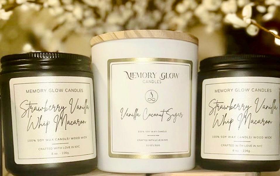 Memory Glow Candles on display, two black jar vessels with cream labels and one white vessel in the middle with gold trim white label and wood lid.