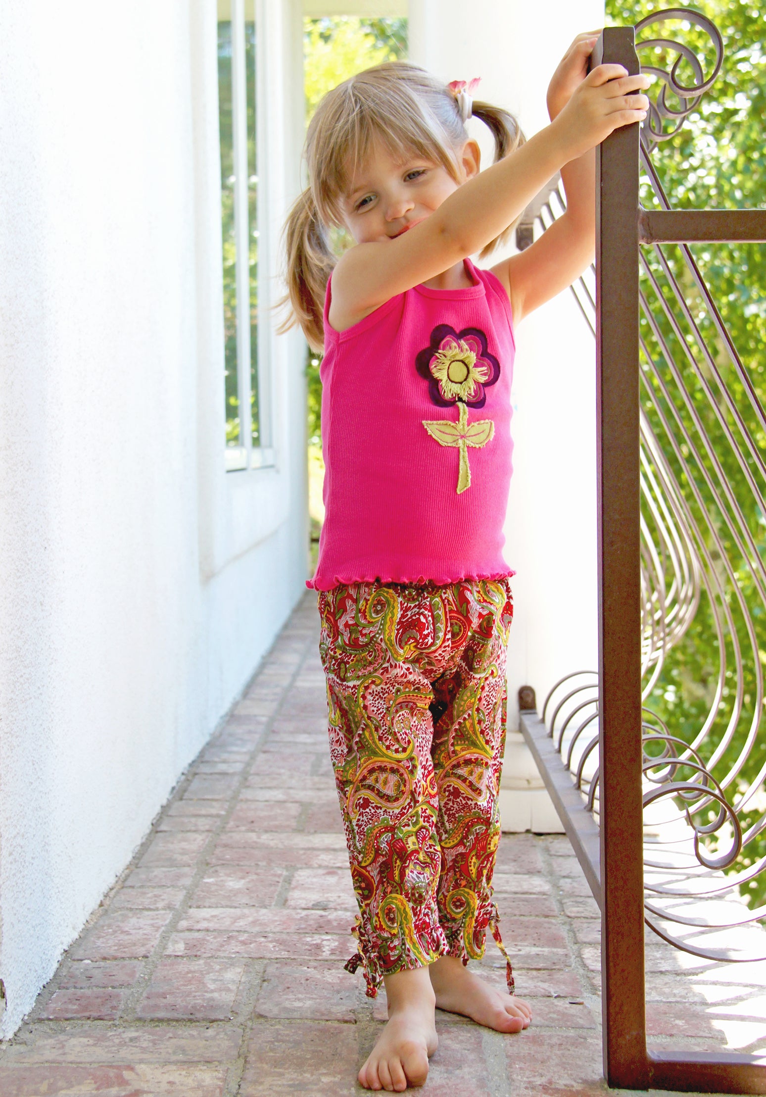 Toddler Girl modeling her flower tank top on a porch. Girls love flowers, and love the soft texture of the hand crafted flower appliques on a comfy, cotton rib knit, tank top. Classic binding around neckline and shoulders, with lettuce trim hem. *These tops sell quickly! If the size/color you need is sold out, send us a request email with the size & color, and your top will be completed in 7 - 10 days. 100% Cotton Wash Cold, turn inside out, Line Dry Consciously made in California