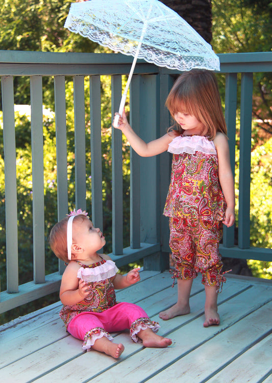 Toddler girl and baby girl in matching outfits on a porch. Gwyneth Girls love to create and play with colors in a fun paisley print halter top. Soft, light weight, cotton woven fabric in an A-line cut halter with delicate ruffle trim, tie back at the neck and soft elastic around the back to stay in place. Pair with the Gwyneth Capri pant for a stunning Spring/Summer look. 100% cotton woven Hand wash or machine wash delicate cycle, cold. Line dry. Sustainably made in California