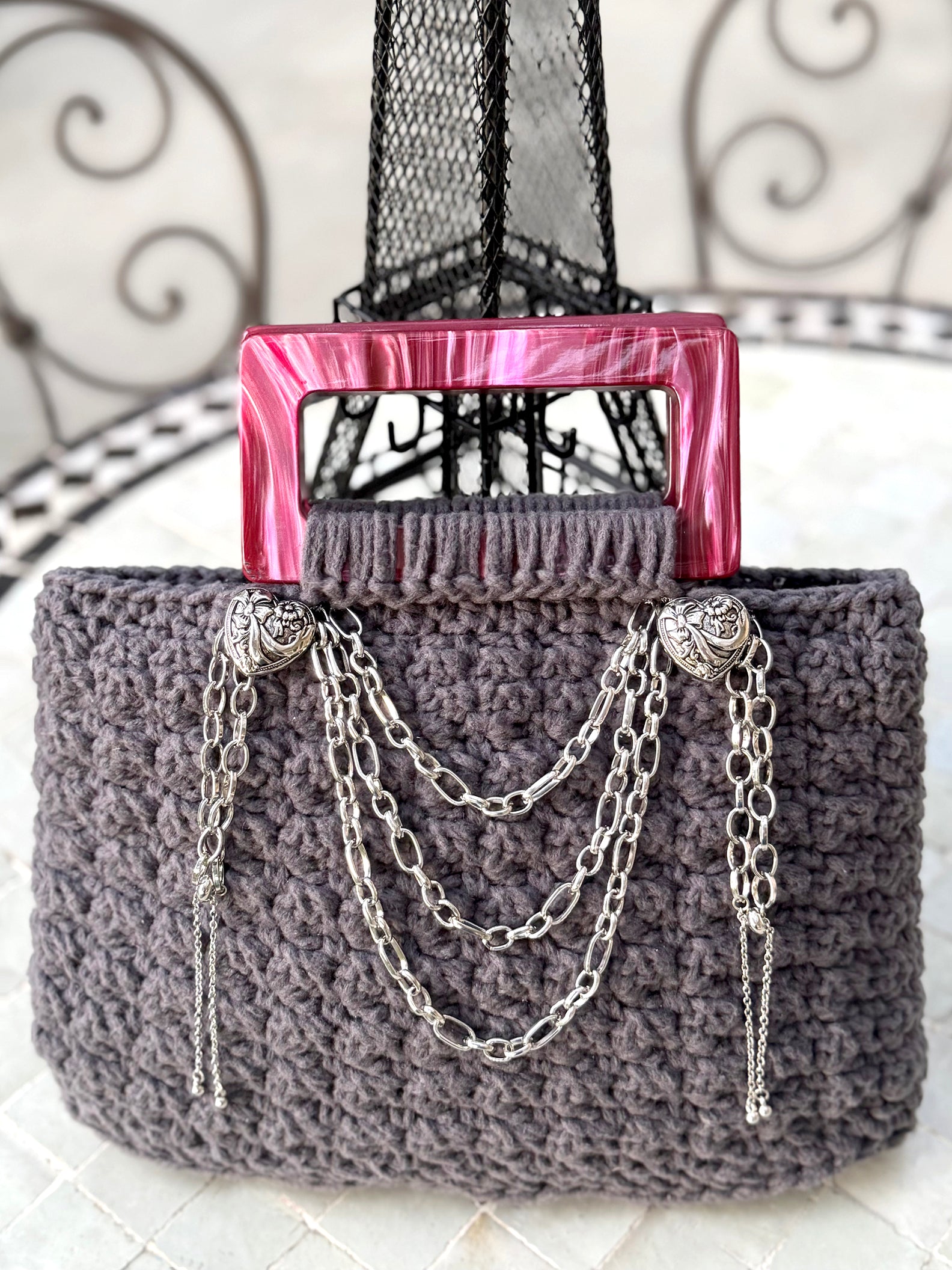 French is the language of Love, and the L'Amour vintage crochet bag reflects the beauty of European expert craftsmanship. Adorned with stainless steel chains, heart engraved buttons, and dark pink, marbled Lucite handles. High quality, upcycled acrylic yarn in slate gray, crocheted in a secure binding pattern, insures no lining is needed. Dimensions: 10" long, 10" high (including handles), 3.5" wide Dry Clean only Consciously made in California