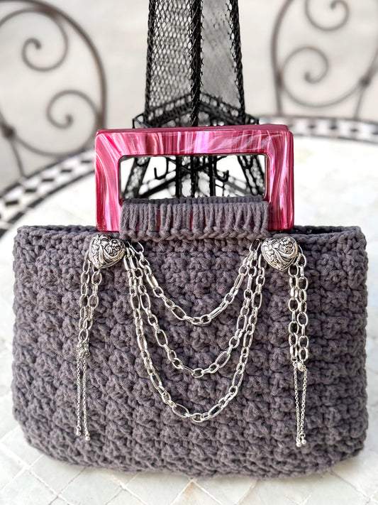 French is the language of Love, and the L'Amour vintage crochet bag reflects the beauty of European expert craftsmanship. Adorned with stainless steel chains, heart engraved buttons, and dark pink, marbled Lucite handles. High quality, upcycled acrylic yarn in slate gray, crocheted in a secure binding pattern, insures no lining is needed. Dimensions: 10" long, 10" high (including handles), 3.5" wide Dry Clean only Consciously made in California