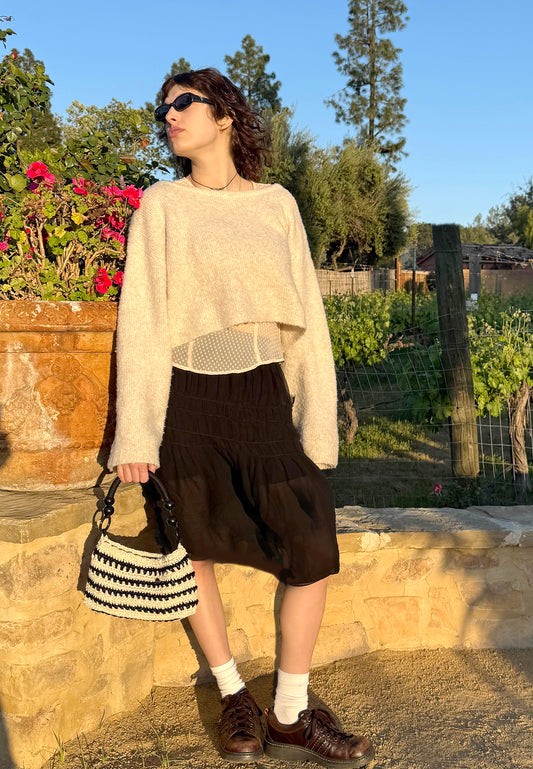 Vintage charm makes this Tropez crochet bag a true statement piece. Hand crocheted with black and cream/gold sparkle, upcycled cotton/nylon blend yarn. Fully lined with side pocket, 70's vintage button closure and flexible black cord wrapped handles, detailed with black wood beads and rings at the ends. Dimensions: Long: 11.5", High: 6" ( 11" with handles), Width: 4" Care: Spot treat with mild soap or dry clean Consciously made in California